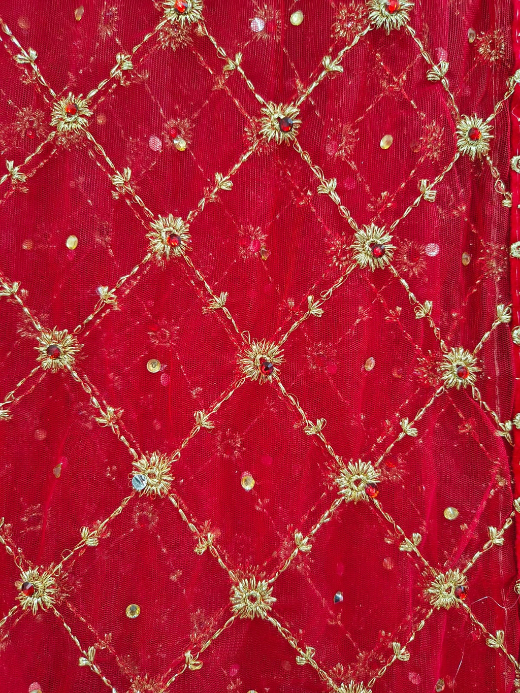 Extreme macro close-up of gold zardozi diamond jaal embroidery on red net dupatta showing gold sunflower motifs and scattered sequins at intersections