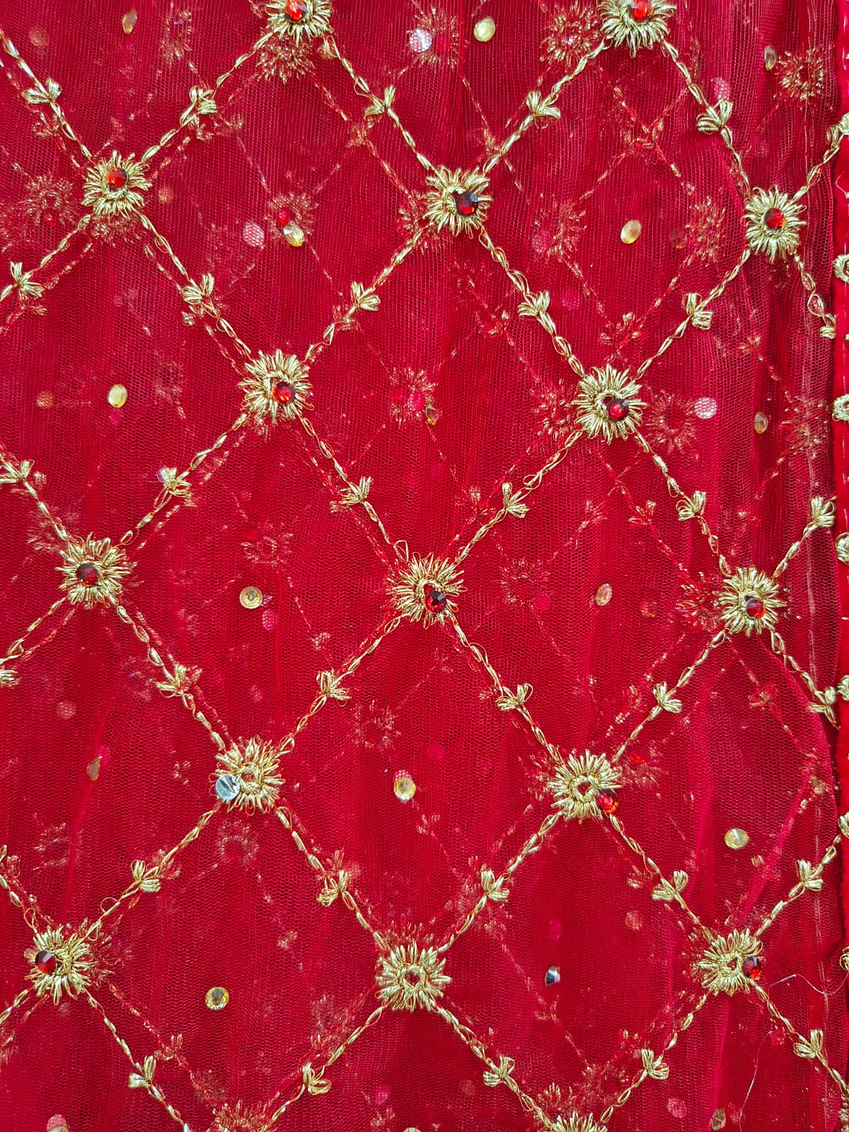 Extreme macro close-up of gold zardozi diamond jaal embroidery on red net dupatta showing gold sunflower motifs and scattered sequins at intersections